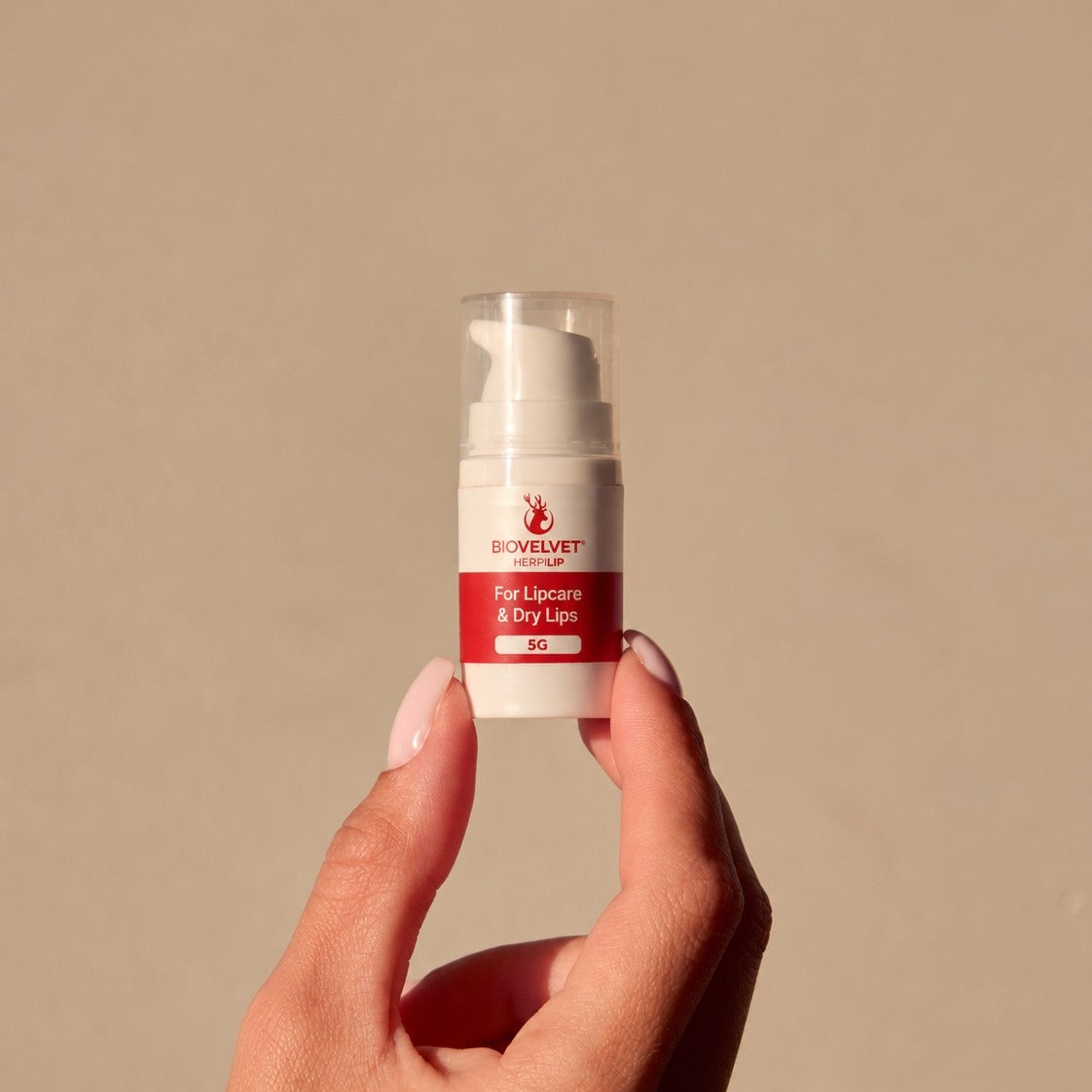 Hand holding the BIOVELVET Herpilip 5g pump in warm sunlight