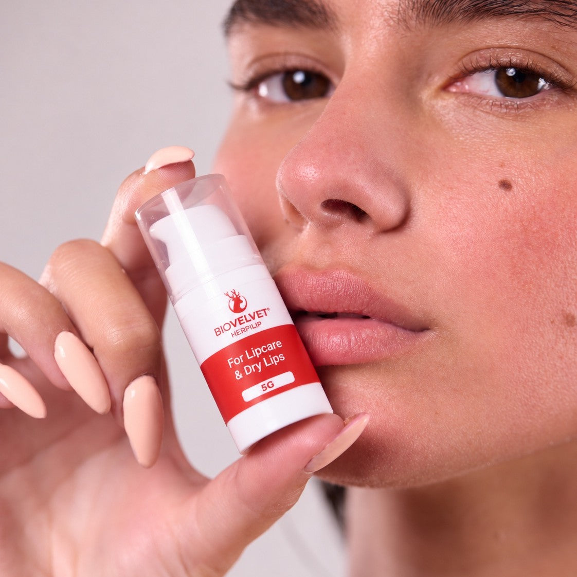 Woman holding BIOVELVET Herpilip lip balm next to her lips